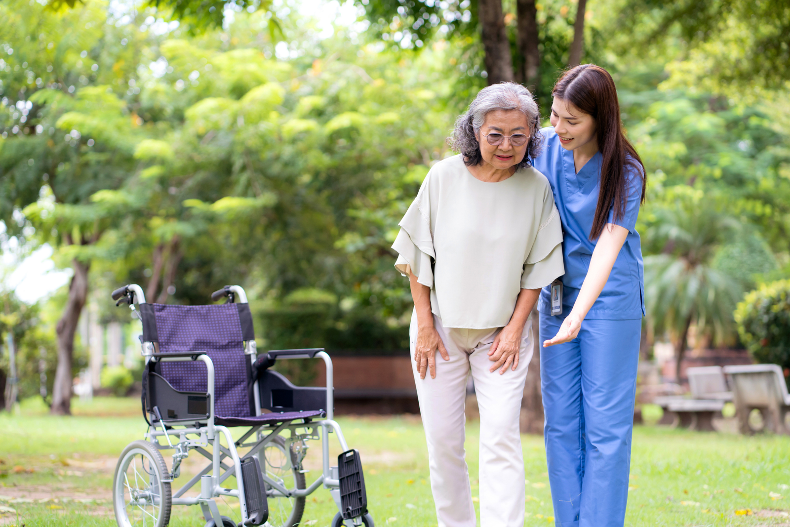 Caregiver helping an elderly woman walk outdoors in a park